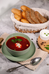 Beetroot soup with sour cream and herbs in a plate, close-up. Tasty and hearty dinner. Borsch with vegetables on a gray background.