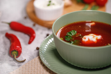 Beetroot soup with sour cream and herbs in a plate, close-up. Tasty and hearty dinner. Borsch with vegetables on a gray background.
