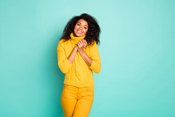 Photo of cute dark skin wavy lady holding hands together overjoyed spring mood wear yellow knitted pullover stylish pants isolated blue teal color background