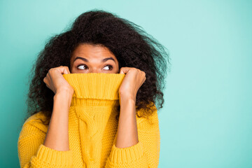 Close up photo of funny dark skin wavy lady hiding half facial expression with collar looking empty space wear yellow knitted pullover isolated teal color background