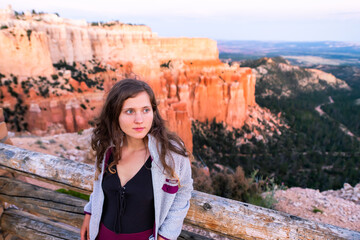 Young woman at Paria view overlook with sunset over hoodoos rock formations in Bryce Canyon National Park leaning on railing