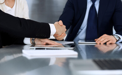 Business people shaking hands after contract signing at the glass desk in modern office. Unknown businessman with colleagues at meeting or negotiation. Teamwork, partnership and handshake concept