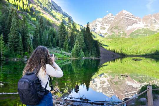 Maroon Bells in Aspen, Colorado in July 2019 summer and mirror reflection at sunrise with woman photographer back taking picture photo
