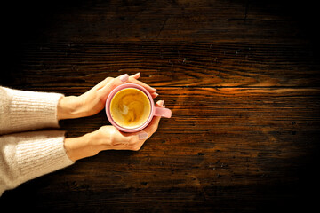 Young female manicured hands holding cups of coffee with fresh foam on dark rustic wooden table background. Free space for your decoration, copy space, top view, flat photo. Cold winter time and Chris