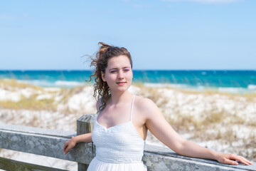 Fototapeta na wymiar Miramar beach ocean in Florida gulf of mexico panhandle with young happy woman girl closed eyes in white dress leaning back on wooden fence