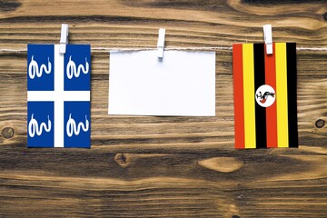 Hanging flags of Martinique and Uganda attached to rope with clothes pins with copy space on white note paper on wooden background.Diplomatic relations between countries.