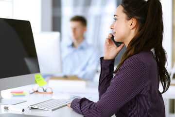 Business woman using computer at workplace in modern office. Brunette secretary or female lawyer smiling and looks happy. Working for pleasure and success