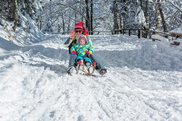 Mother and daughter speeding downhill on wooden sledge.