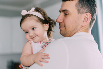 Little smiling girl in arms of her young father at home