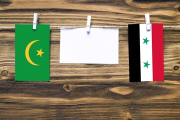 Hanging flags of Mauritania and Syria attached to rope with clothes pins with copy space on white...