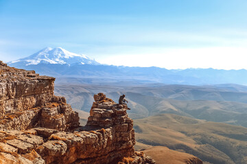 A young man is sitting on a cliff. Elbrus view. Caucasian ridge. Mountain landscape. sunny day