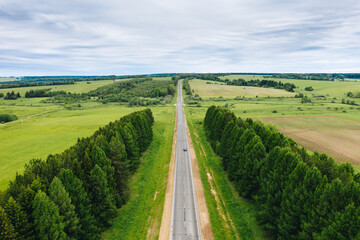 Fototapeta na wymiar Aerial view of straight country road between green trees and fields in summer day. Rural landscape in Udmurtia, Russia