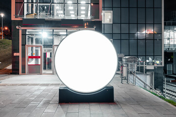 Blank round white outdoor banner stand next to bright modern building of railway metro station.