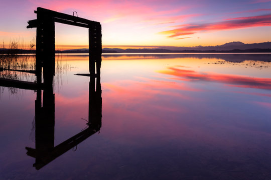 Monte Rosa and the remaining of an old boathouse reflecting on Lake Varese during a winter sunset at Calcinate del Pesce, Varese Province, Lombardy, Italy.