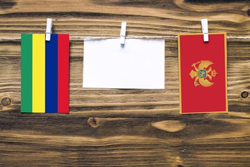 Hanging flags of Mauritius and Montenegro attached to rope with clothes pins with copy space on white note paper on wooden background.Diplomatic relations between countries.