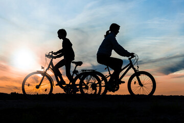 Fototapeta na wymiar Boy and young girl riding bikes in different directions, silhouettes of riding persons at sunset in nature