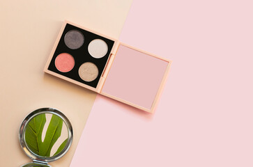 Neutrals eye shadow palette on a beige and pink colour block background with mirror reflecting  monstera leaf with copy space