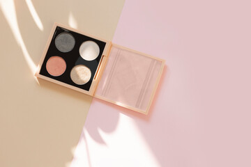 Eye shadow palette on a color block beige and pastel pink background with a monstera leaf shadow with copy space