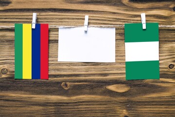 Hanging flags of Mauritius and Nigeria attached to rope with clothes pins with copy space on white note paper on wooden background.Diplomatic relations between countries.