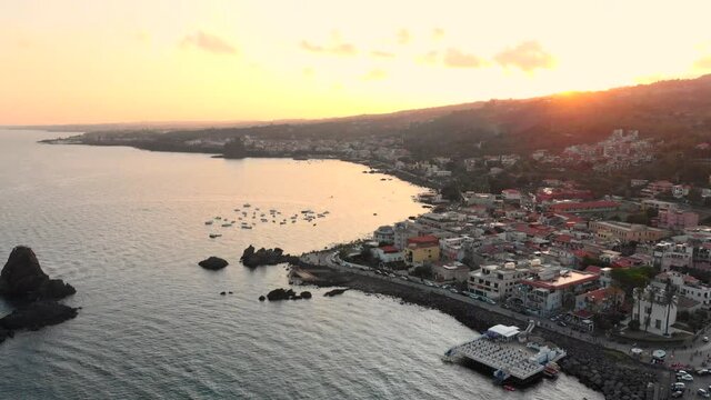 Sunset aerial pan above sea of Aci Trezza fishing village in Italy