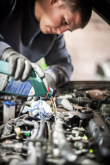 Auto mechanic repairer pours new motor oil into car engine
