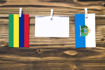 Hanging flags of Mauritius and San Marino attached to rope with clothes pins with copy space on white note paper on wooden background.Diplomatic relations between countries.