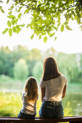 Rear view of young mother and small daughter sitting on the bench in park