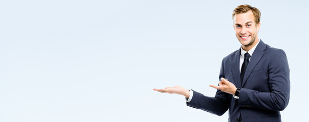 Smiling businessman showing something, isolated over grey background. Copy space for some slogan or...