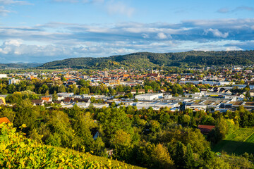 Obraz premium Germany, Wide aerial view above houses, church and roofs of schorndorf city in valley between forested hills in warm evening sunset light
