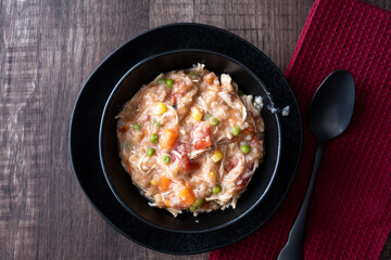 Puerto Rican Chicken Rice Soup in a black stoneware bowl and saucer on a dark wood table, black metal spoon, maroon cloth napkin