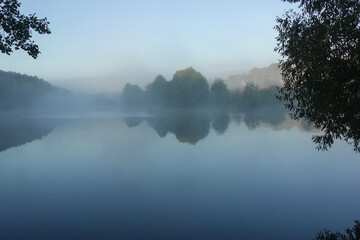 Early morning on the lake. Fog above the water. The shore is covered with trees.