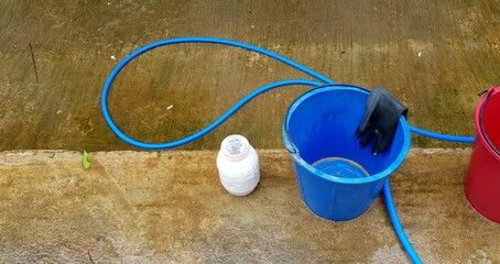 Blue and red bucket with black rubber glove and can of washing powder on wet floor after cleaning with copy space  