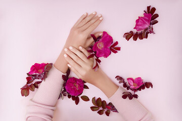 Hand with pink flowers and petals lying on a paper background. Cosmetics for hand skin care. Natural petal cosmetics, essential oils, anti-wrinkle and anti-aging hand care