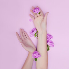 Hand with pink flowers and petals lying on a paper background. Cosmetics for hand skin care. Natural petal cosmetics, essential oils, anti-wrinkle and anti-aging hand care