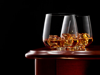 Two glasses of whiskey and ice on the wooden table. Low key.