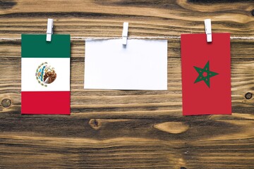 Hanging flags of Mexico and Morocco attached to rope with clothes pins with copy space on white note paper on wooden background.Diplomatic relations between countries.