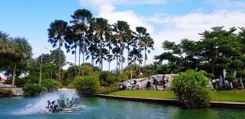 Hydraulic turbine or water vane for increase oxygen and  Adjust water balance in lake or pool with coconut, palm, rock and blue sky background at Wat Luang Phor Toh temple, Nakhonratchasim, Thailand.