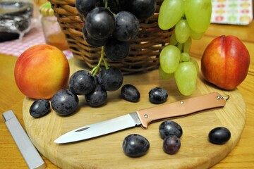 Folding knife and fresh organic ripe fruits peaches grape natural gourmet product dessert 
