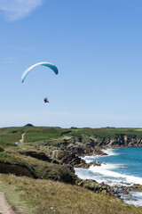 Fototapeta na wymiar paraglider flying above a picturesque sandy beach on te rocky coast of Brittany
