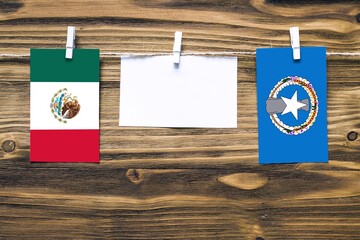 Hanging flags of Mexico and Northern Mariana Islands attached to rope with clothes pins with copy space on white note paper on wooden background.Diplomatic relations between countries.