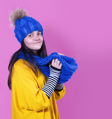 Young brunette in a blue hat with a scarf on a pink background
