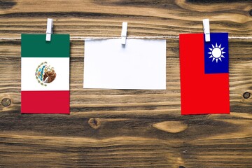 Hanging flags of Mexico and Taiwan attached to rope with clothes pins with copy space on white note paper on wooden background.Diplomatic relations between countries.