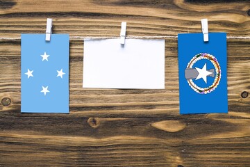 Hanging flags of Micronesia and Northern Mariana Islands attached to rope with clothes pins with copy space on white note paper on wooden background.Diplomatic relations between countries.