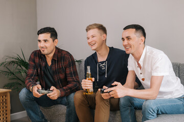 Three handsome young friends having fun on evening playing video games with excellent mood in...