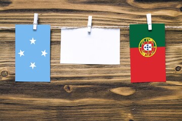 Hanging flags of Micronesia and Portugal attached to rope with clothes pins with copy space on white note paper on wooden background.Diplomatic relations between countries.