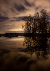 Long exposure of trees and reflective water at cloudy night.