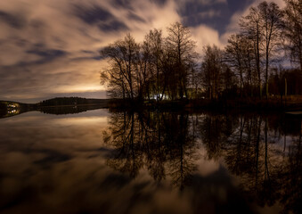 Panoramic long exposure of trees and reflective water at night.