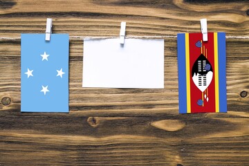Hanging flags of Micronesia and Swaziland attached to rope with clothes pins with copy space on white note paper on wooden background.Diplomatic relations between countries.