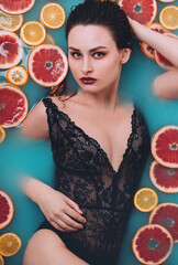 Young beautiful woman take a bath with fruits. Laing in blue water with citrus slices. Home spa
