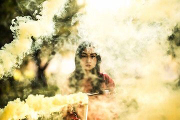Young asian woman holding yellow colorful smoke bomb on the outdoor park. Yellow smoke spreading